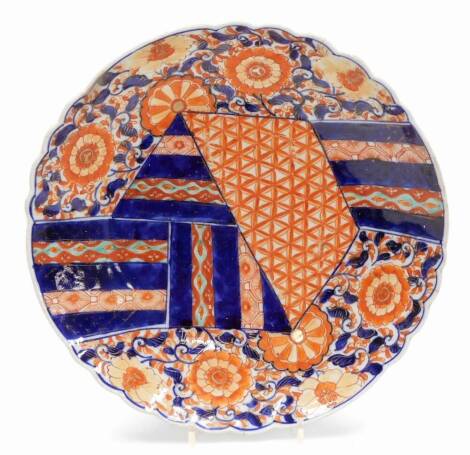 A 19thC Imari dish, of floral circular form, profusely decorated with flowers and a geometric pattern predominately in orange and blue, with floral decoration verso, and single line mark to the circular foot, 32cm wide. (AF)