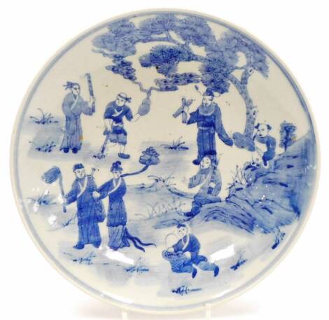 A Chinese blue and white plate, profusely decorated with figures before trees, with a double line border, Xangxi style seal mark beneath, but later, 31cm diameter.