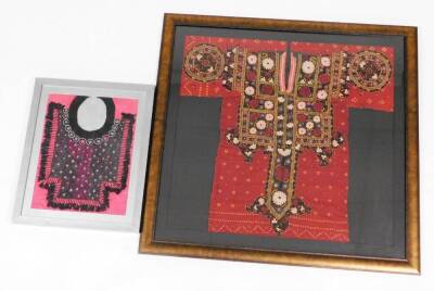 An Indian batik and embroidery panel, of a kaftan design with panels of flower head designs on a red cotton, 74cm x 79cm, framed and glazed, and another small garment sample on pink silk, framed and glazed. (2)