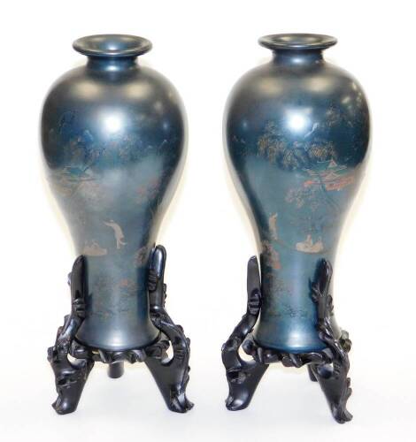 A pair of early 20thC Japanese lacquer vases, each of a dark blue colour with figures boating on a river below trees and pavillions, 30cm high, on wooden bases of a further 7cm (AF). (2)