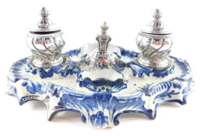 A Continental faience blue and white pottery desk stand, of serpentine form, with a pair of spiral fluted hinged ink wells, painted B C mark, 31cm wide.