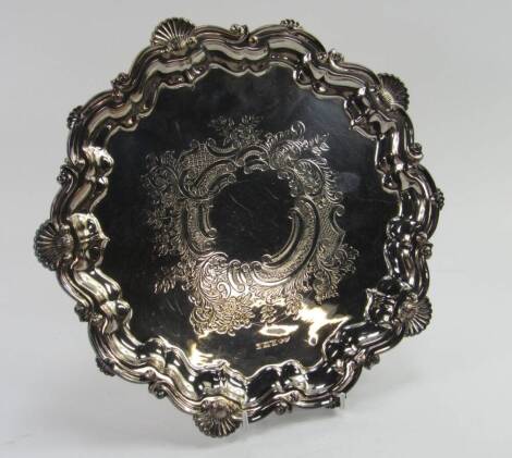 A silver pie crust salver, with a border of scallop shells and rococo scrolls, central engraved rococo decoration, raised on three scroll feet, Birmingham 1980, 28.3t oz.