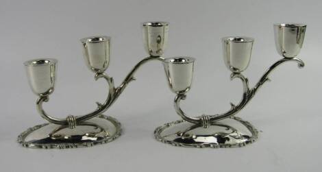 A pair of Mexican silver three branch candelabra, of graduated form on a tear drop base with gadrooned rococo scroll rim, 33.75t oz.