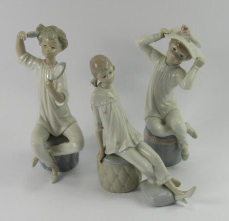 Three Lladro porcelain figures of girls, seated on pouffes, one brushing her hair, another relaxing and the third adjusting her hat, printed marks.