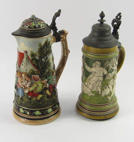 A German pottery musical stein, early 20thC, relief moulded with figure drinking, dancing and playing music, 1/2L, 27cm high, and a further pottery stein, with pewter mounts, relief decorated with a scene of village entertainment, 27.5cm high.