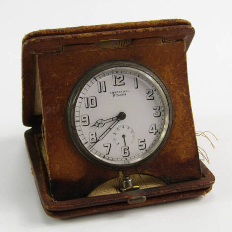 A Tiffany & Co travel clock, white enamel dial bearing Arabic numerals, subsidiary eight day dial, Longines eight day movement, No 3795549, in a tan leather strut case.