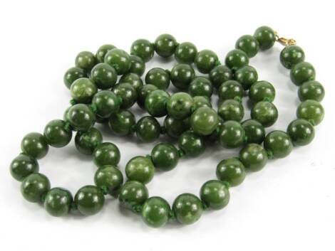 A string of sixty five jade beads, on a yellow metal clasp, stamped 9ct.