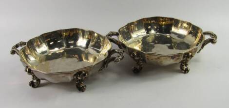 A pair of plated serving dishes, of twin handled fluted circular form raised on four rococo scroll feet, 33cm diameter.