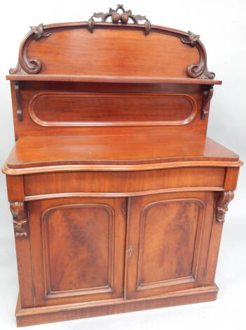 A Victorian mahogany serpentine chiffonier, with carved and moulded back and two flamed arch panel door base on plinth, 112cm wide