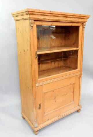 A 19thC stripped pine cabinet, with moulded cornice, glazed upper door and panelled lower on ball feet, 104cm wide x 107cm high