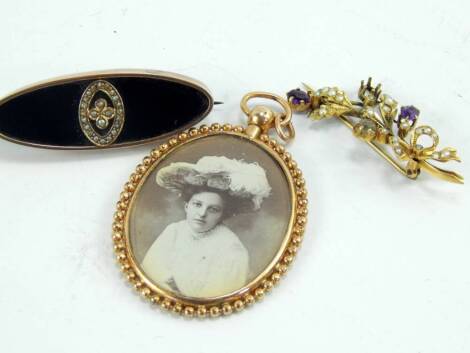 A Victorian onyx seed pearl and rose gold oval mourning brooch, a seed pearl and amethyst set yellow metal spray brooch, and a yellow metal pendant locket, (3).