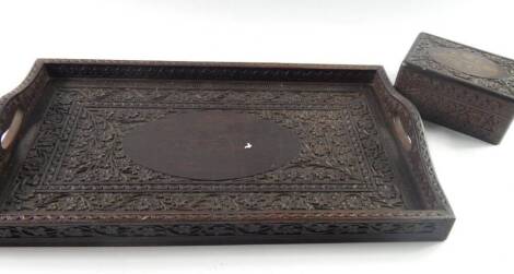 An Indian hardwood tray, 20thC, of twin handled, rectangular form carved with flowers, 48cm x 27.5cm, together with a box, similarly carved, with an oval relief to the lid brass inlaid with leaves and berries, 15cm x 10cm x 7cm, (2).