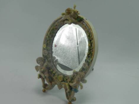 A Sitzendorf porcelain strut mirror, of oval form encrusted with flowers and surmounted with cherubs, 33cm x 20cm, (AF).