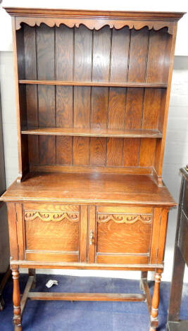 A 1930's oak dresser, with plate rack top, two panelled doors and turned legs, 93cm wide.