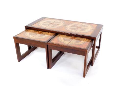 A vintage mahogany tile top nest of occasional tables, set with orange and brown tiles in a geometric cloud design, raised on U shaped end supports, comprising one long table, 51cm high, 96.5cm wide, 48cm deep., enclosing a pair of smaller square tables, 