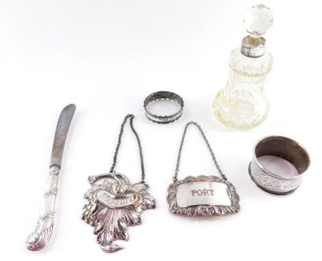 A George V cut glass scent bottle and stopper, with silver collar, Birmingham 1911., cake knife with silver pistol handle, Sheffield 1911., two silver napkin rings, Continental brandy label, and a Sheffield plate port label. (6)