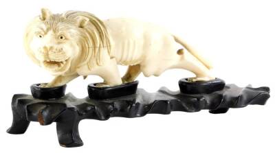 A 19thC oriental carved ivory figure of a prowling lion, (AF), 16cm long, on contemporary hardwood stand.