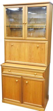 A teak side cabinet in the Nathan style, with two glazed doors including a shelf, and a fall front for cocktails, the base with a frieze drawer and two panelled doors, on a plinth, 184cm high, 83cm wide, 32cm deep.