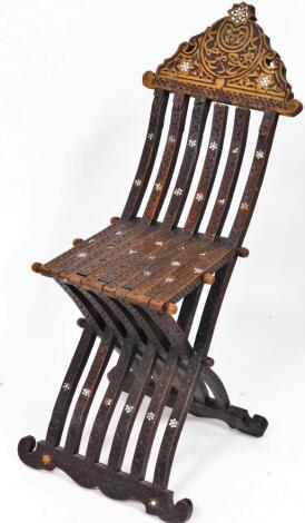 A Syrian hardwood folding chair, with a shaped scroll back and six pronged articulated centre on scroll feet, profusely carved with flower heads, lettering and further scrolls with a mother of pearl inlay (when open) 105cm high, 34cm wide, 32cm deep.(AF)