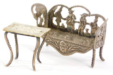 A Dutch white metal miniature settee, decorated with cherubs playing musical instruments, dog, figures in Dutch costume playing instruments, etc., import marks for London, and a miniature table, with a mother of pearl top, decorated with leaves and an etc