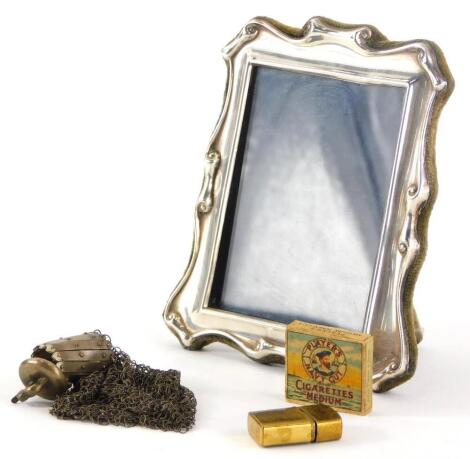 An Elizabeth II silver framed photograph frame, with scroll border, Sheffield 1990, 12cm high, a miniature brass cigarette lighter, miniature Players Navy Cut cigarette box, and a metal coin purse, the top cast with an elephant. (4)