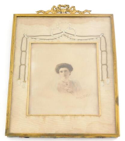 An Edwardian hand tinted photograph, indistinctly signed ?Coliages, in the form of a lady wearing a shawl with flower, etc., the elaborate gilt brass frame embellished with swags of silk, etc., 37cm x 23.5cm.