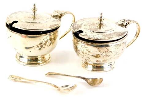 Two George V silver mustard pots, of plain form, with blue glass liner, Birmingham 1937 and 1939, and two silver mustard spoons, weighable silver 3oz, 6cm high. (AF)