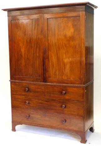 A early Victorian mahogany linen press, with a moulded cornice and two panelled doors enclosing sliding trays, the base with two short and two long drawers, each with turned wooden handles, on bracket feet, 213cm high, 150cm wide.