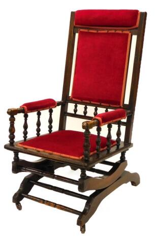 A late 19thC American style walnut rocking chair, with a red velvet padded back, arm rest and seat, on sprung X-shaped end supports with castors.