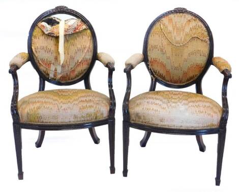 A pair of continental mahogany open armchairs in French style, each with an oval back, carved with wheat ears, and bell flowers within beaded moulded borders, with a padded back, arm rest and seat, with scrolled arm shaped supports, a bow fronted seat rai