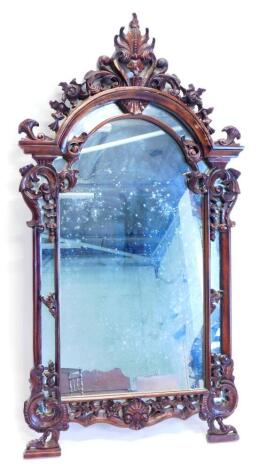 A mahogany wall mirror in rococo style, carved with flowers, scrolls etc., around an arched plate, 146cm high, 76cm wide.