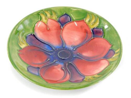 A Moorcroft pottery pin tray, decorated centrally with an anemone flower, on a green ground, 12cm diameter.