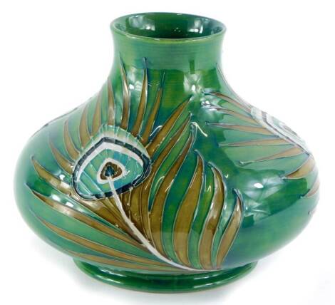 A Moorcroft squat baluster pottery vase, decorated with peacock feathers, on a green ground, 16cm high.