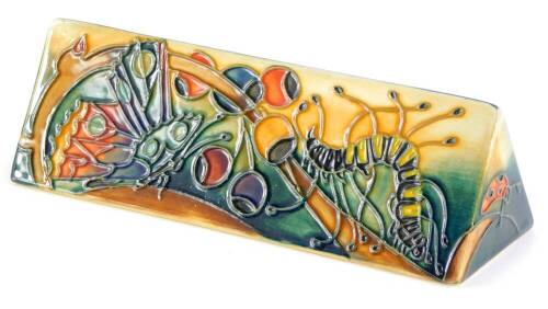 A Moorcroft pottery triangular plaque, decorated to the reverse with berries, butterflies, caterpillars, etc., 19cm wide.