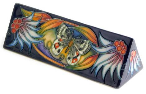 A Moorcroft pottery triangular plaque, decorated to one side with a central butterfly, flanked by two flowers, 18.5cm wide.