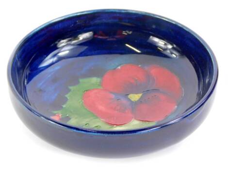 A Moorcroft pottery shallow bowl, decorated with a pansy, on a blue ground, 11.5cm diameter.