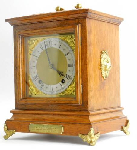 A late 19thC oak cased mantel clock, with patent brass movement, with a square dial, applied with gilt spandrels and with a silver chapter ring, engraved with Roman numerals, the case with loop handle and gilt bracket feet, presentation inscription presen