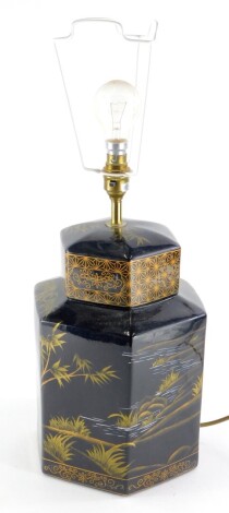 An oriental style pottery lamp base, decorated with river landscapes etc., in black on a gilt ground, to simulate a 19thC tea caddy, the base 30cm high, 41cm high to the top of the light fitting.