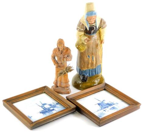 A continental pottery figure of a Dutch lady, unmarked (AF), 34cm high, a small carved wooden figure of a Dutch lady carrying faggots, 22cm high, and a pair of Delft plaques (4).