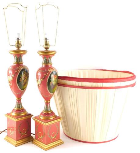 A pair of baluster shaped table lamp bases, each painted with a fruit, flowers, swags etc., on a pink ground with a square base and two pleated shades, the lamps 51cm high to the top of the brass lighting fitting. Buyers Note: This lot contains untested o