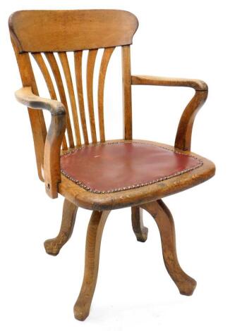 A mid 20thC oak swivel office chair, with a pierced back, a brown leatherette padded seat on splayed legs.