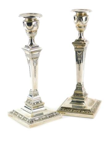 A pair of Edwardian silver candlesticks, each cast with swags, patera, etc., in Adam style, with a circular sconce, on a tapering column and stepped square base, loaded, London 1905, label to underside for Lambert 12 Coventry Street, 29cm high.