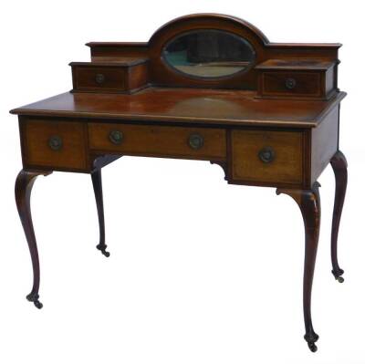 An Edwardian mahogany desk, the raised back with a central oval bevelled mirror plate, flanked by two trinket drawers, the chequer strung base with a moulded edge and three drawers around and a shaped apron on cabriole legs, with pad feet and castors, 106