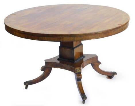 A Regency rosewood and brass inlaid breakfast table, the circular top decorated with scrolls, leaves etc., on a tapering column and concave platform, with splayed legs, terminating in brass paw castors, 122cm deep.