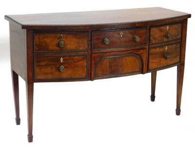 A George III mahogany bow fronted sideboard, the top with an ebony strung border and a gadrooned edge, above two central drawers, flanked by a celibate drawer and a door, on square tapering legs, with splayed feet, 91cm high, 148cm wide, 64cm diameter.