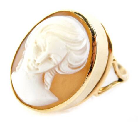 A shell cameo dress ring, with oval cameo depicting a maiden quarter profile, in rub over setting, 2.5cm high, on a thin applied V splayed shoulder band, yellow metal, unmarked, ring size S, 6g all in.