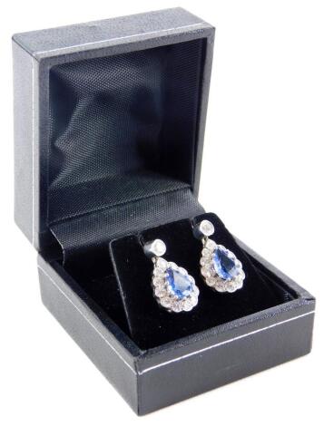 A pair of sapphire and diamond teardrop earrings, with central teardrop cut, pale blue sapphire, in a white gold claw setting, the stone measuring 7.2mm x 5.6mm x 2.4mm, surrounded by various twelve round brilliant cut tiny diamonds, each measuring 1.8mm 