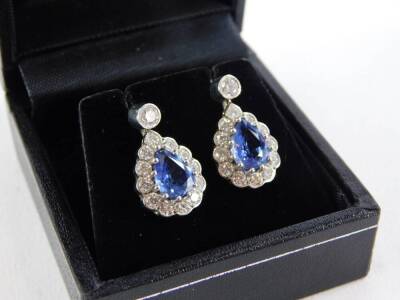 A pair of sapphire and diamond teardrop earrings, with central teardrop cut, pale blue sapphire, in a white gold claw setting, the stone measuring 7.2mm x 5.6mm x 2.4mm, surrounded by various twelve round brilliant cut tiny diamonds, each measuring 1.8mm - 2