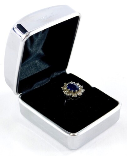 A sapphire and diamond floral cluster ring, the central oval cut sapphire measuring 8.8mm x 6.6mm x 2.8mm, in a white gold claw setting, surrounded by ten round brilliant cut diamonds, each 2.8mm x 2mm, in a raised basket setting on white metal band with