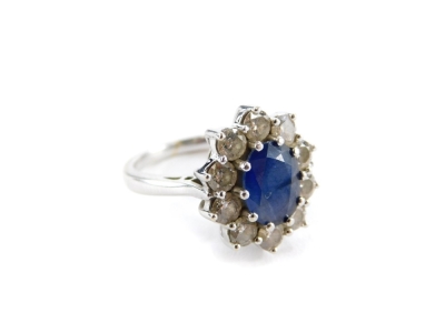 A sapphire and diamond floral cluster ring, the central oval cut sapphire measuring 8.8mm x 6.6mm x 2.8mm, in a white gold claw setting, surrounded by ten round brilliant cut diamonds, each 2.8mm x 2mm, in a raised basket setting on white metal band with - 2